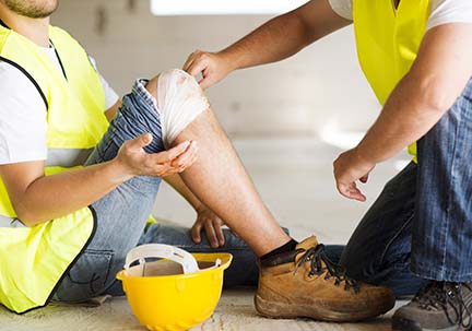 A construction worker is fixing a bandage on a fellow workers knee